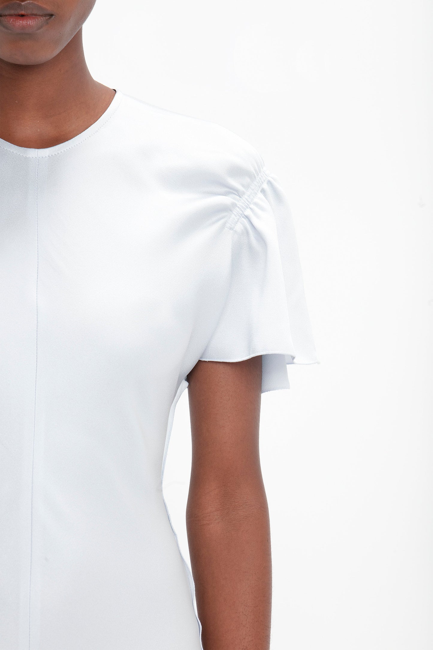 Close-up of a person wearing a plain, light-colored Gathered Sleeve Midi Dress In Ice by Victoria Beckham. The background is white, and the image shows the person from the upper torso to just above the elbow, highlighting an elegant midi dress-inspired look.