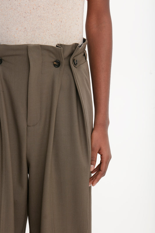 Close-up of a person wearing high-waisted, pleated, olive-green trousers with two buttons in the front, paired with a Victoria Beckham Short Sleeve Top In Nougat.