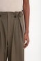 Close-up of a person wearing high-waisted, pleated, olive-green trousers with two buttons in the front, paired with a Victoria Beckham Short Sleeve Top In Nougat.