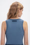 A person with wavy, light brown hair is seen from the back, wearing a sleeveless, ribbed Victoria Beckham Fine Knit Micro Stripe Tank In Heritage Blue.