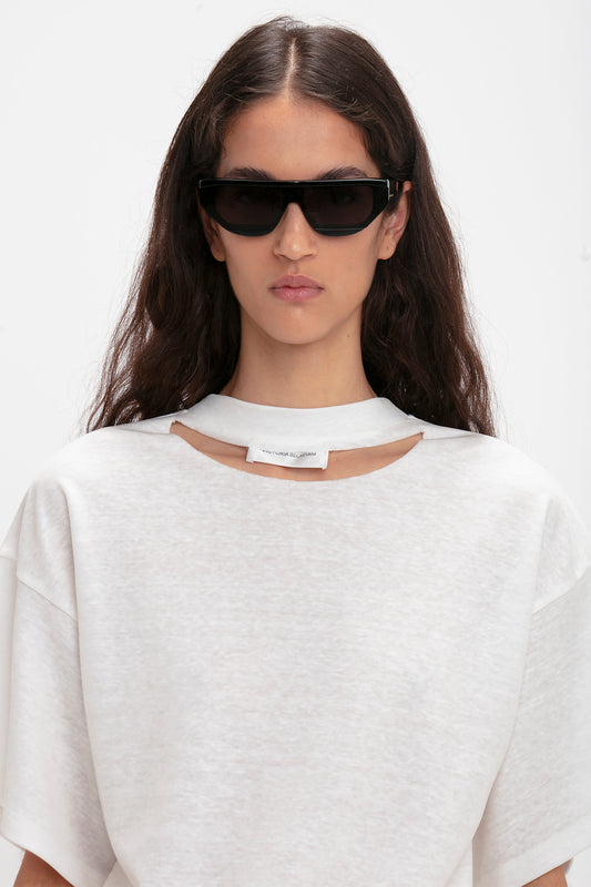 A person with long dark hair wearing a white top and large black Layered Lens Visor Sunglasses In Black from Victoria Beckham.