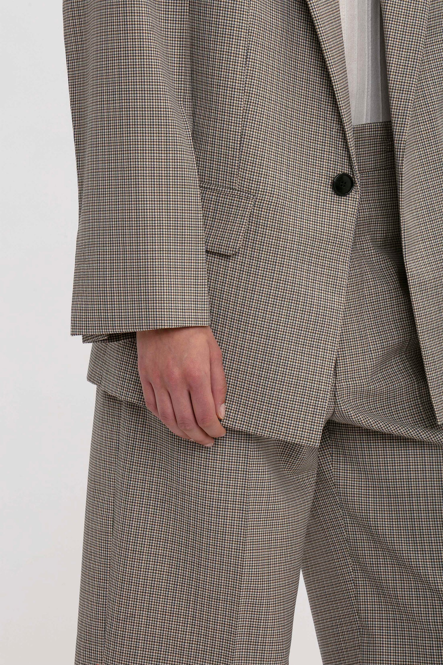 Close-up of a person wearing an oversized gray plaid suit jacket and matching trousers, with their hand partially visible by their side. The Peak Lapel Jacket In Multi by Victoria Beckham enhances the oversized silhouette, adding a touch of modern elegance.