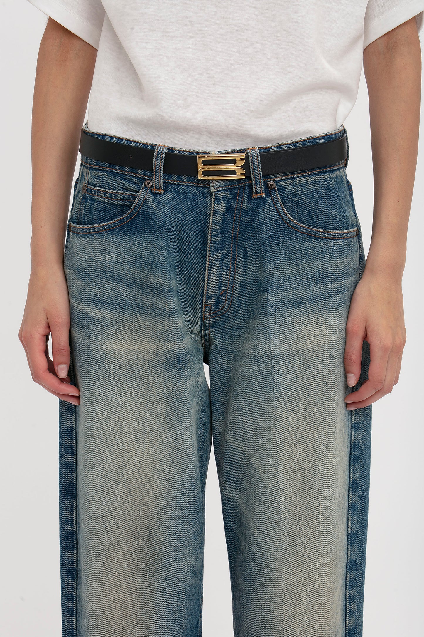 Close-up of a person wearing blue jeans with a Victoria Beckham Exclusive Frame Belt In Midnight Navy Leather, focusing on the waist area against a white background.