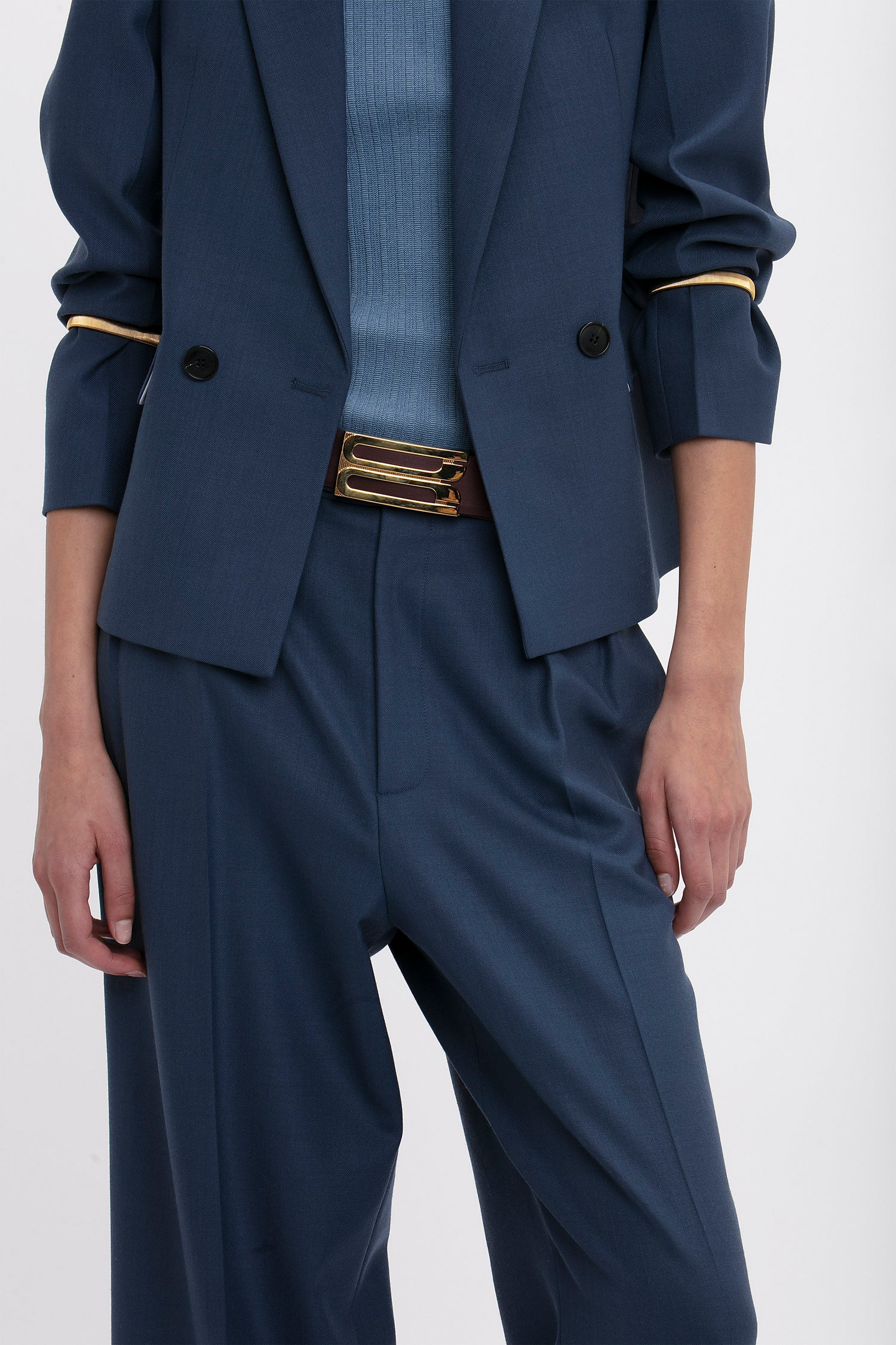 Person wearing a blue suit and matching sweater with Sleeve Cuffs In Gold by Victoria Beckham, a brown belt with gold-plated brass accents, showcasing versatile styling.