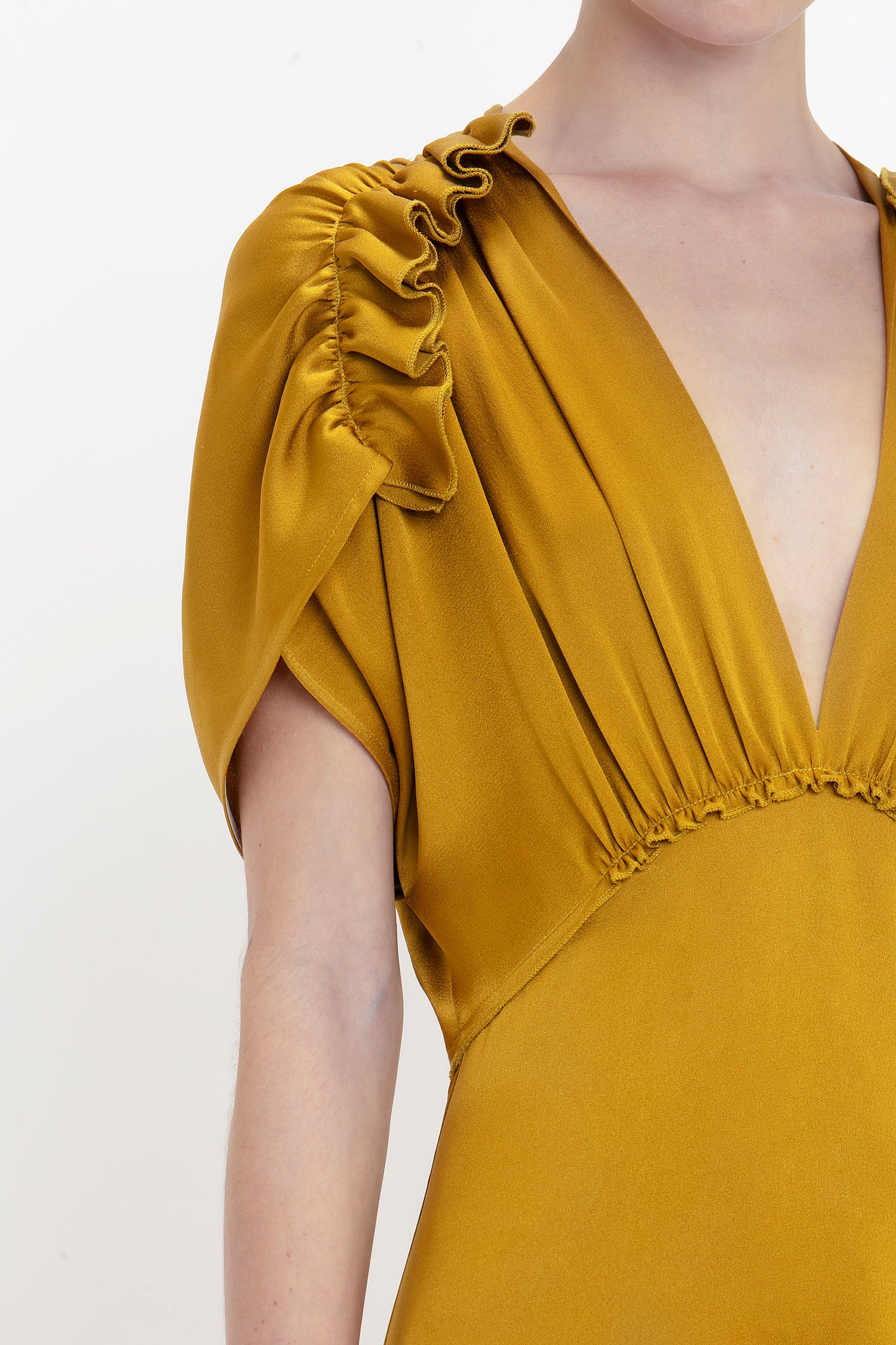 Close-up of a person wearing a Victoria Beckham V-Neck Ruffle Midi Dress In Harvest Gold with ruffled shoulder details and a deep V-neckline. The dress features gathered fabric below the bust, adding a seductive quality to its elegant design.