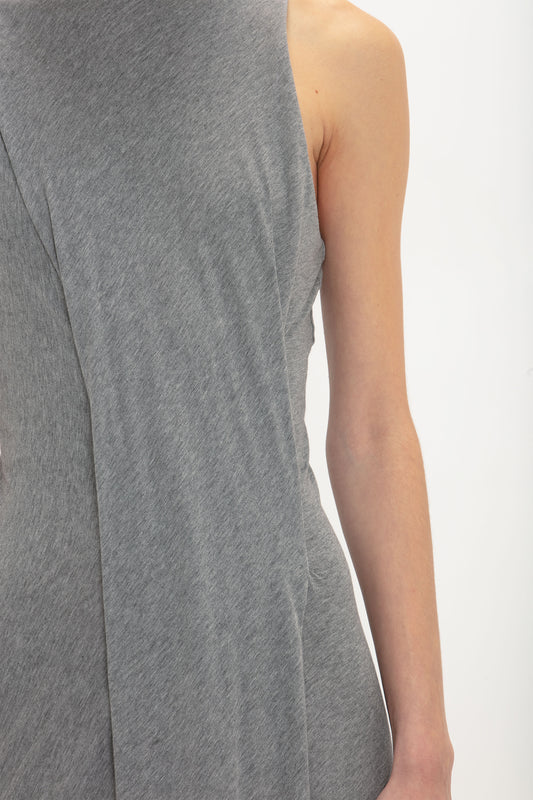 Close-up of a person wearing a sleeveless, asymmetrical Frame Detailed Maxi Dress In Titanium by Victoria Beckham, with the dress covering the front and part of the side.