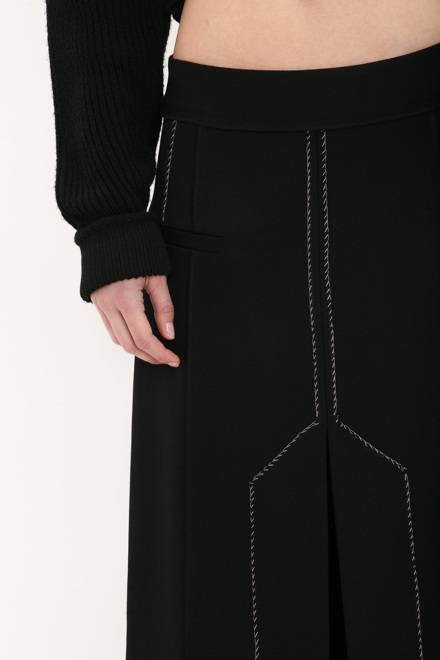 Close-up image of a person wearing a black outfit with visible white stitching details. The ensemble features a black long sleeve garment and a Deconstructed Floor-Length Skirt In Black by Victoria Beckham, creating an elongating silhouette with prominent seam lines.