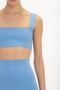 A person wearing a blue Strap Bandeau Top In Marina and matching high-waisted fitted midi skirt from Victoria Beckham stands against a plain white background. The image is cropped at the collarbone and just above the knees.