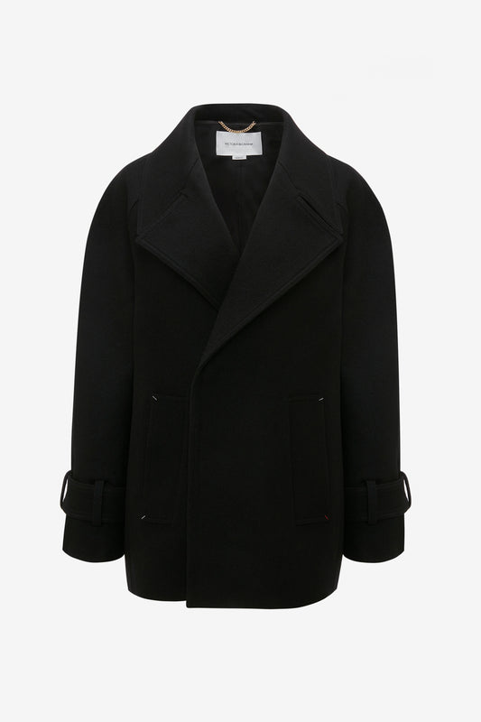 Oversized Pea Coat In Black by Victoria Beckham with wide lapels and flap pockets, showcasing masculine tailoring and adjustable strap details on the sleeves.