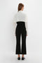 A person is standing with their back to the camera, wearing a white Oversized Bow Detail Blouse In Vanilla by Victoria Beckham and black pants, with black shoes. The feminine flourish of the bow adds a dramatic finishing touch to their outfit.