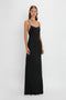 Person standing against a white background, wearing the Victoria Beckham Floor-Length Cami Dress In Black with thin straps.