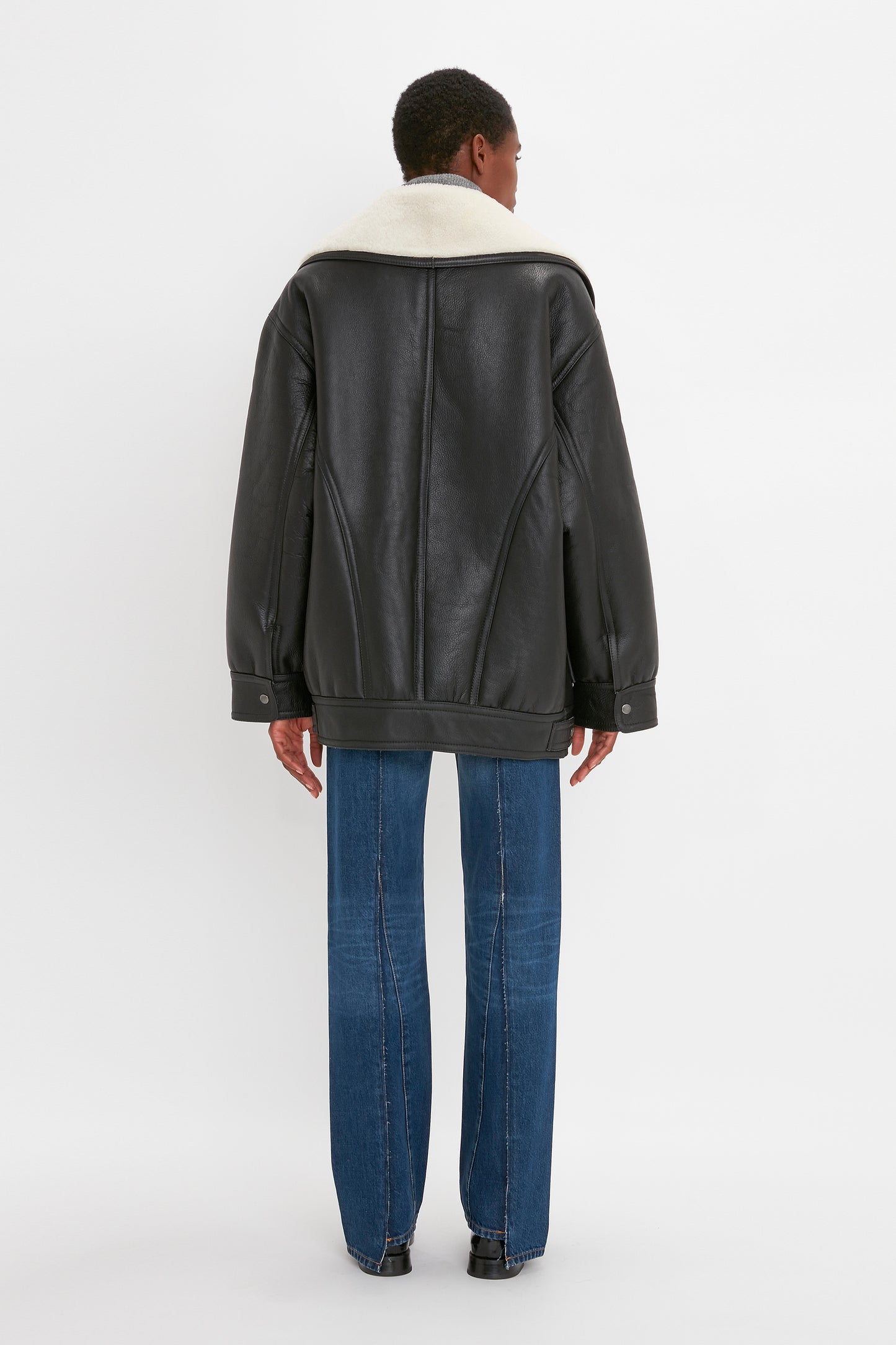 Individual facing away, donning an oversized silhouette of a Shearling Coat In Monochrome by Victoria Beckham and blue jeans.