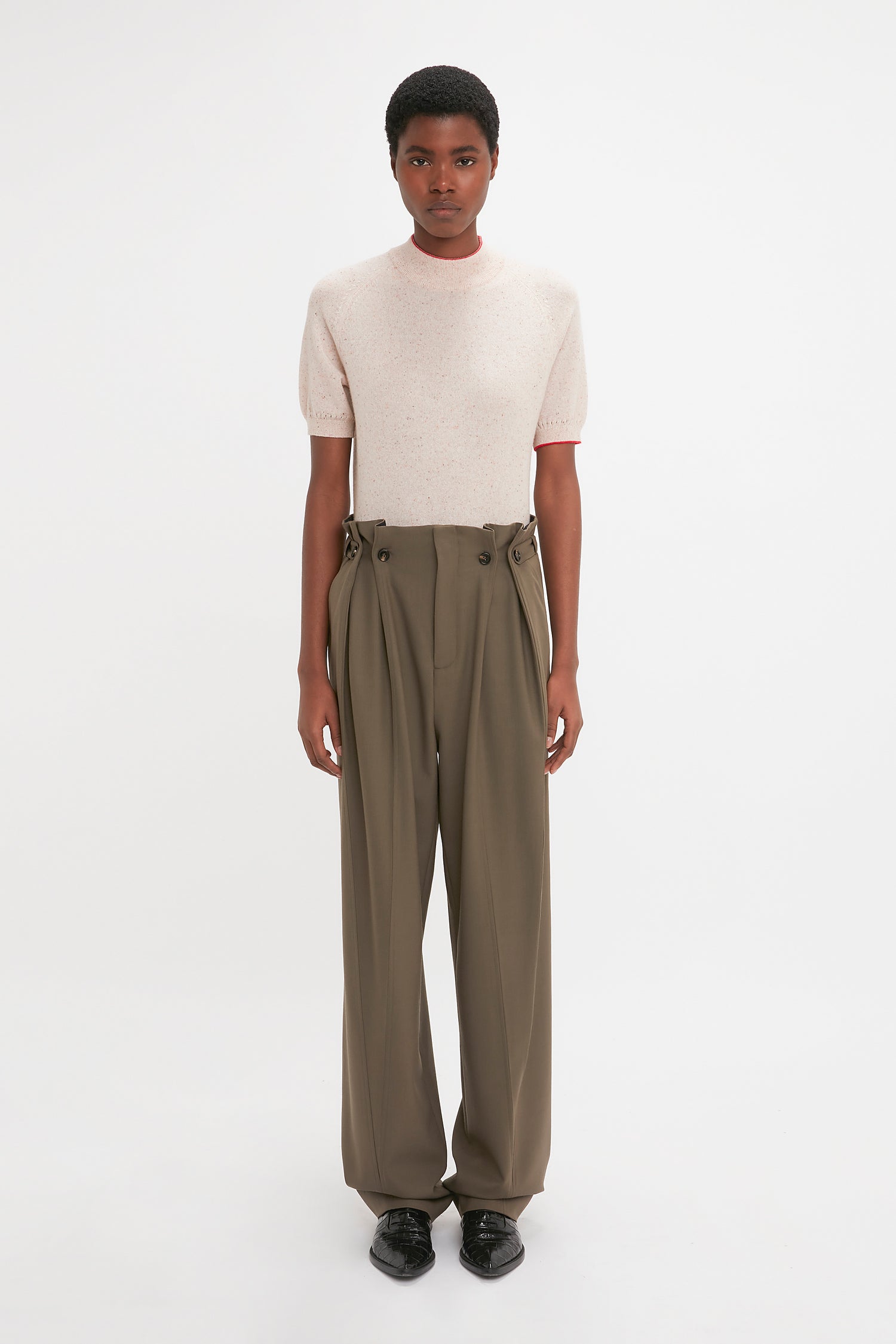 A person wearing the Victoria Beckham Short Sleeve Top In Nougat and high-waisted, wide-legged olive-green trousers stands against a plain white background.