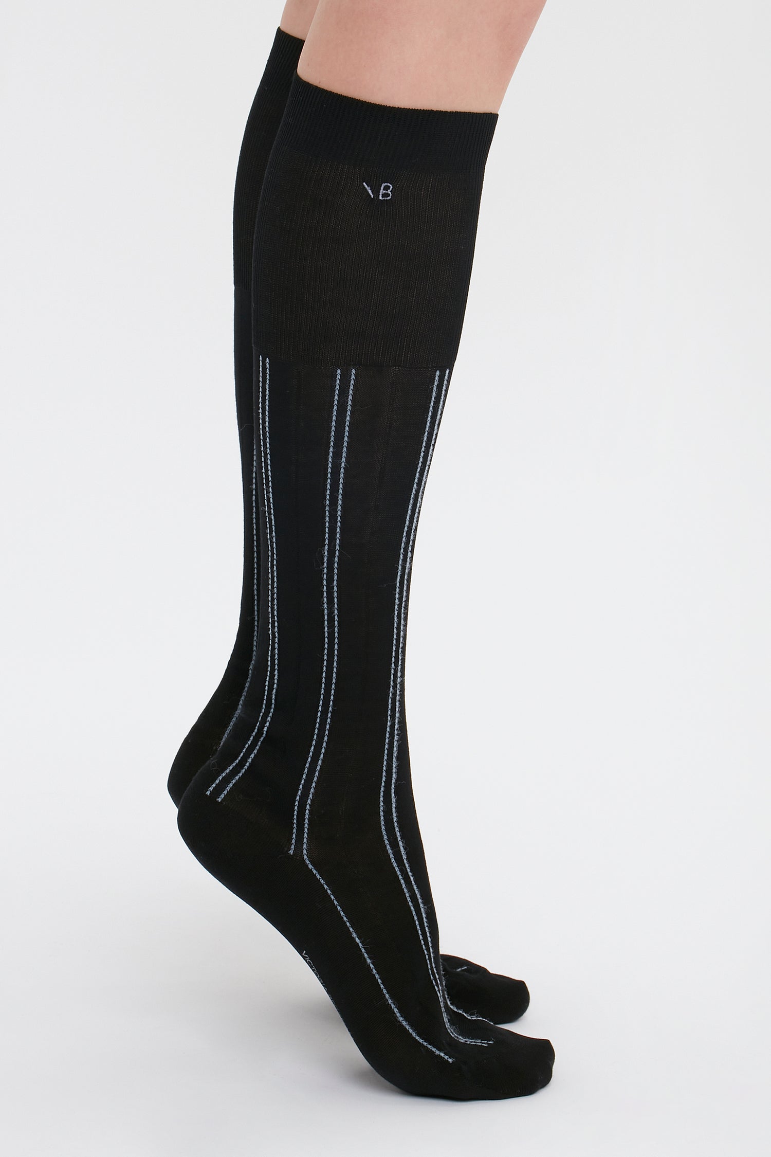 Person wearing Victoria Beckham Superfine Rib Socks In Black, made from 100% cotton, standing on tiptoe against a plain white background.