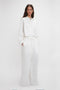 A woman in Victoria Beckham's chic Drawstring Pyjama Trouser In Washed White with an adjustable drawstring waistband, standing against a plain light background.