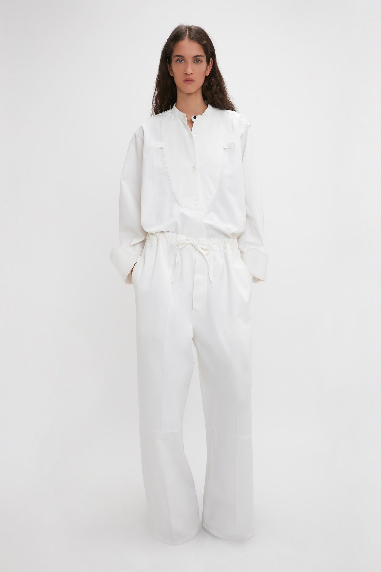 A woman in Victoria Beckham's drawstring pyjama trouser in washed white, with wide-leg trousers and cinched waist, standing against a plain light background.