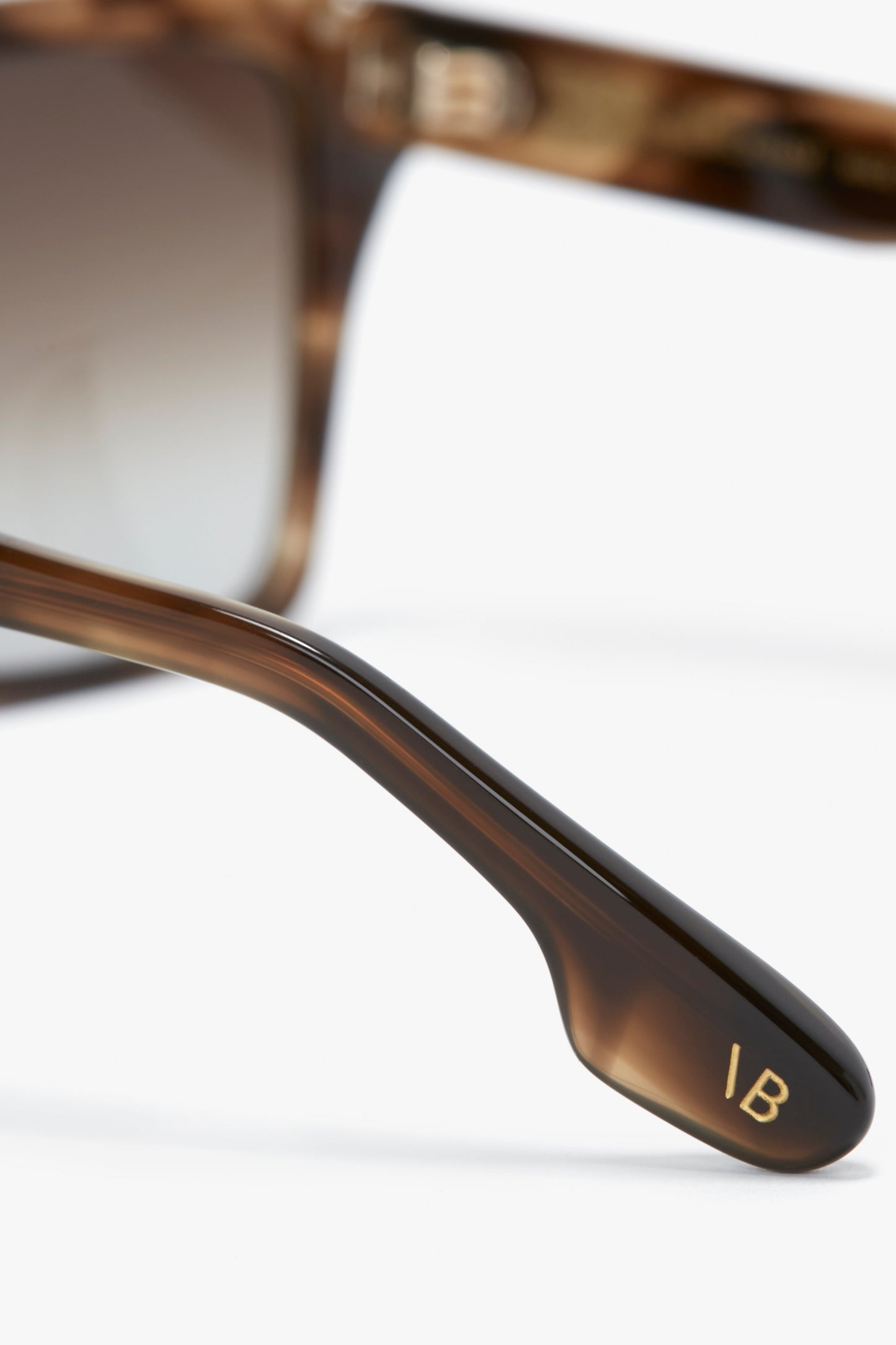 Close-up of a brown, contemporary **Soft Square Frame Sunglasses In Striped Khaki Havana** with gradient lenses. The arm of the sunglasses displays a gold "IB" logo, revealing its exclusive **Victoria Beckham** eyewear label.