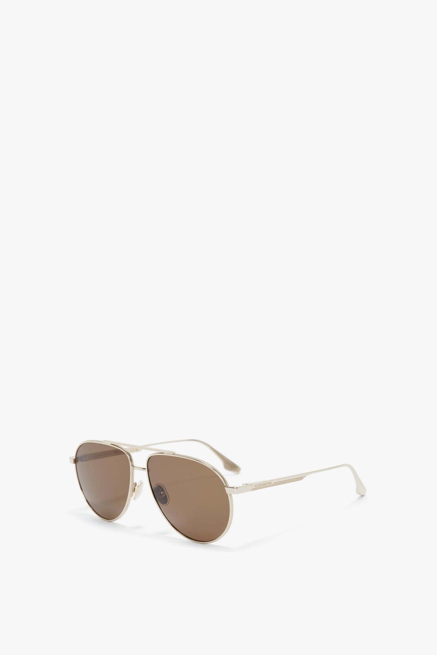 A pair of V Metal Pilot Sunglasses In Gold-Khaki by Victoria Beckham, with aviator-style gold frames and brown lenses, featuring adjustable nose pads for added comfort, displayed on a white background.