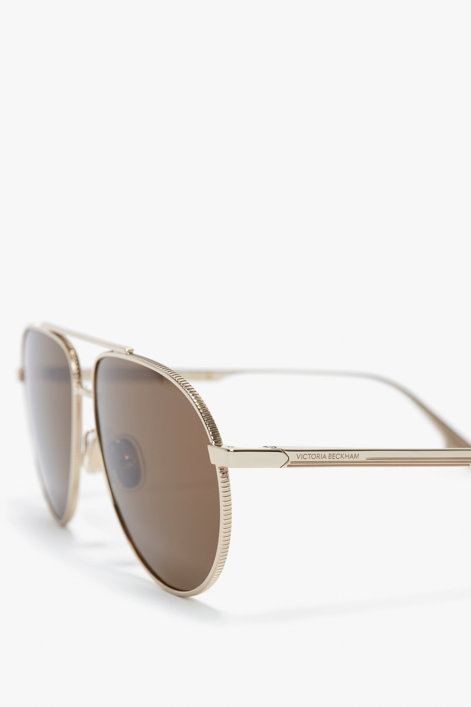 Close-up of gold/khaki aviator-style V Metal Pilot Sunglasses In Gold-Khaki with metal frames and dark lenses, featuring adjustable nose pads and a small Victoria Beckham logo on the temples.