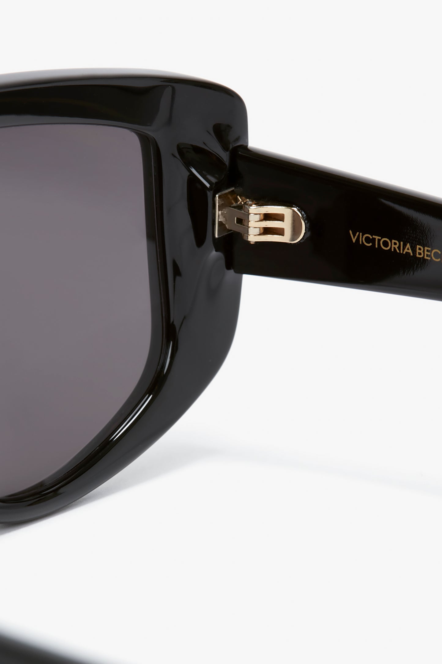 Close-up of Victoria Beckham eyewear, showcasing Acetate Visor Sunglasses In Black with dark lenses, displaying the gold-colored hinge and "Victoria" inscribed on the temple.