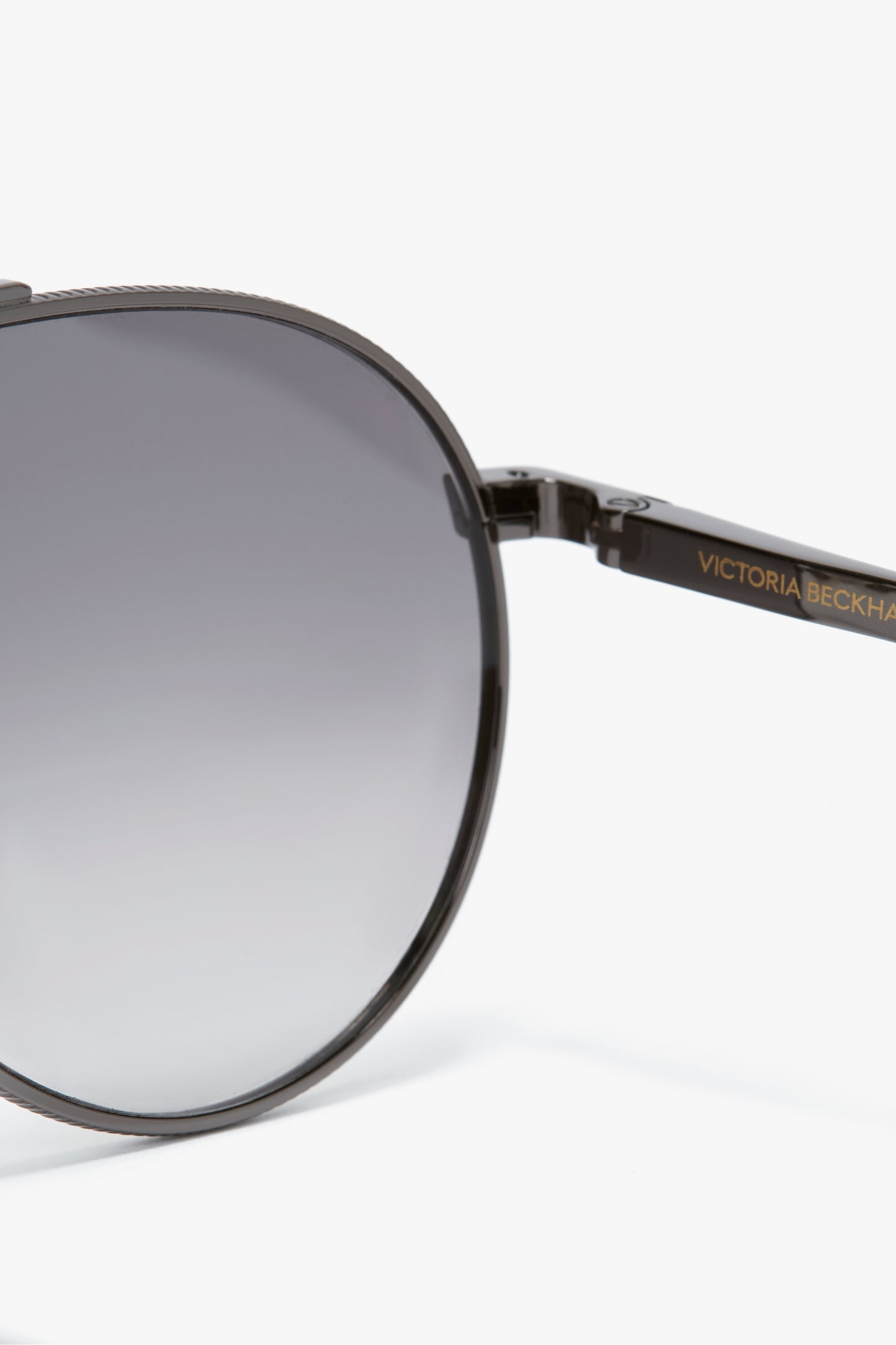 Close-up of V Metal Pilot Sunglasses In Grey Gradient featuring a gunmetal grey gradient design and "Victoria Beckham" branding on the arm.