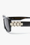 Close-up of Victoria Beckham Chain Detail Rectangular Frame Sunglasses In Black featuring a modern eyewear design, showcasing black rectangular frames with an elegant gold chain link detail on the temple arm, set against a white background.