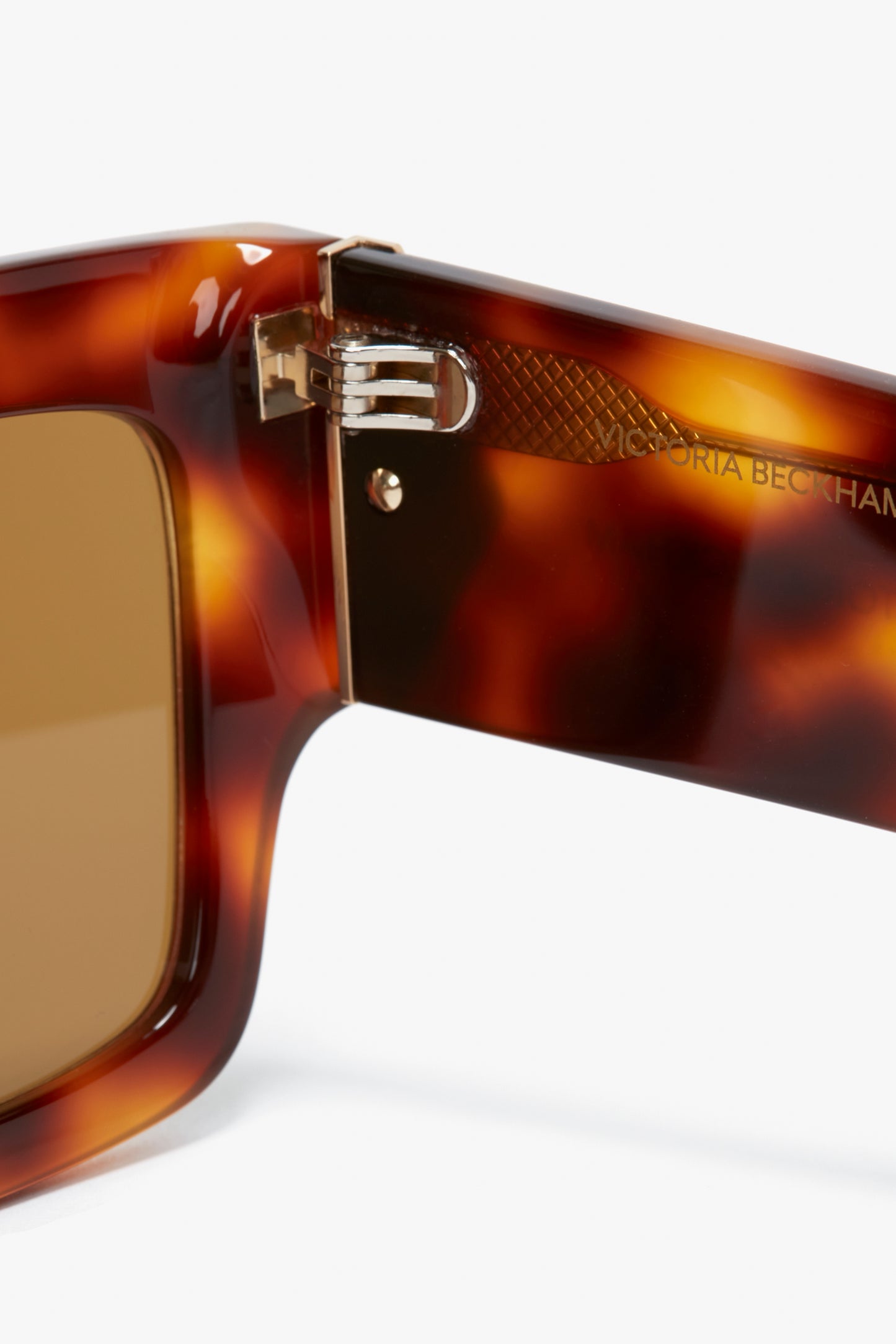 Close-up of the hinge and frame of V Plaque Rectangular Frame Sunglasses In Tortoise, featuring "Victoria Beckham" engraved on the inner side.