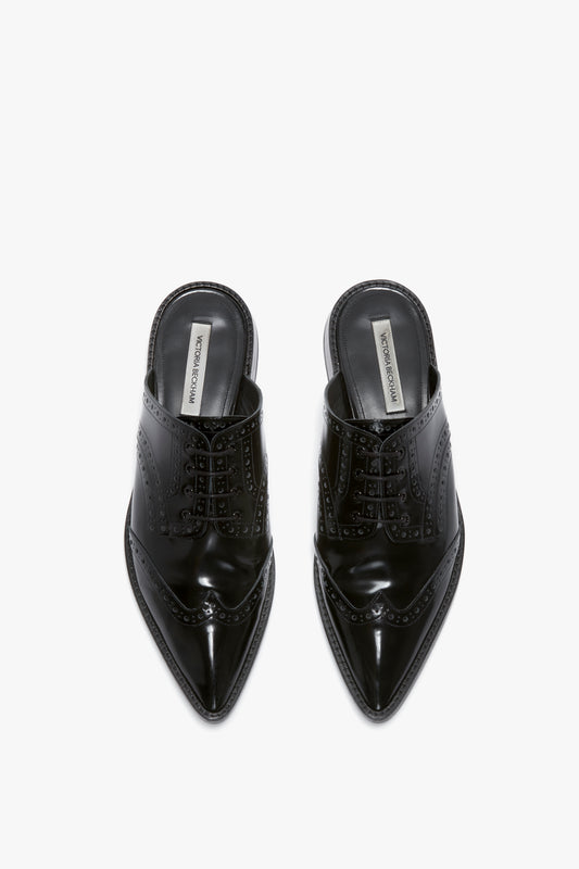 Top view of a pair of Victoria Beckham Flat Lace Up Mules In Black Leather with intricate perforated detailing and pointed toes, crafted from luxurious calfskin and featuring insole branding.