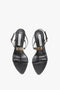 A pair of Victoria Beckham Frame Detail Sandal In Black Leather with thin straps and metallic buckle accents, featuring an adjustable ankle strap and sculptural heel, all on a white background.