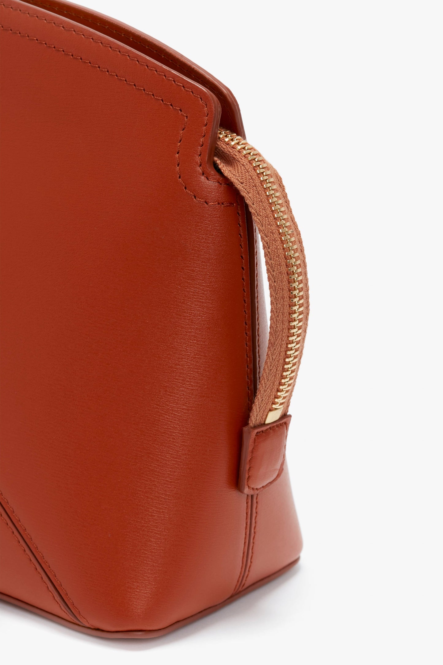 Close-up of a Victoria Beckham Victoria Clutch Bag In Tan Leather crafted from glossy calf leather, featuring a gold zipper detail and structured design.