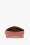 A Victoria Beckham Victoria Clutch Bag In Tan Leather with an open top, revealing a beige interior, a zippered pocket, and a leather strap on the side.