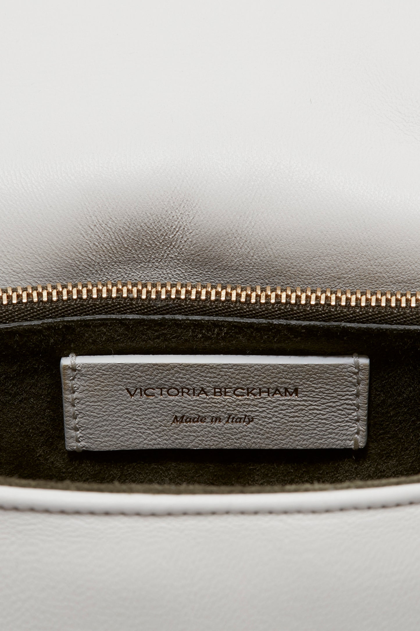 The interior label of a white leather Puffy Chain Pouch Bag With Strap In White Leather showing the text "Victoria Beckham Made in Italy" above the zipper, complemented by a detachable shoulder strap with gold chain detail.