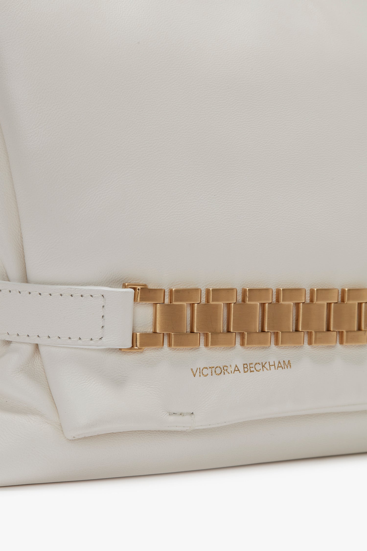 Close-up of a white leather Puffy Chain Pouch Bag With Strap In White Leather featuring a gold chain detail and "Victoria Beckham" embossed in gold.