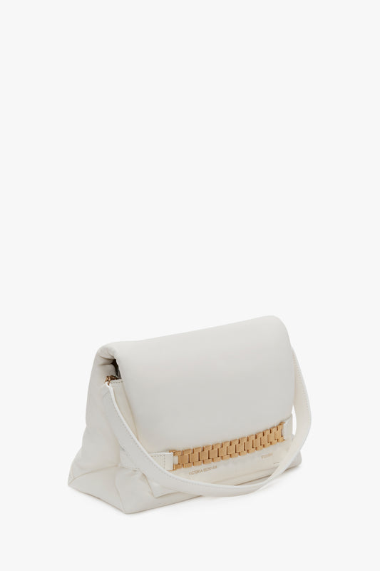 A Victoria Beckham Puffy Chain Pouch Bag With Strap In White Leather with a fold-over flap and a gold chain detail rests against a plain white background.