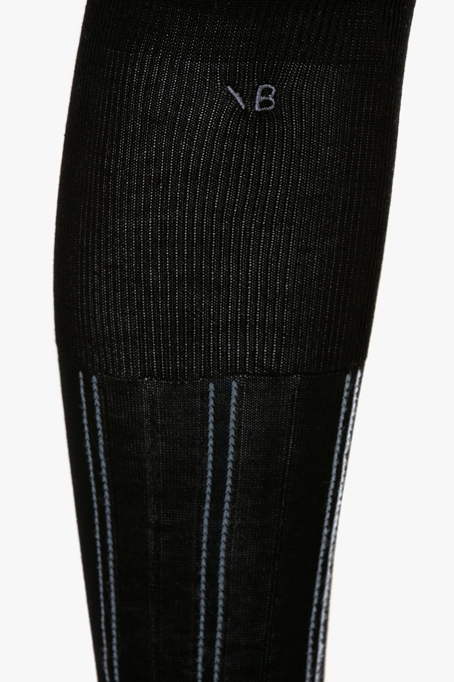 Close-up of a black and steel blue superfine ribbed sock with vertical white and blue striped details. The letters "VB" are embroidered near the top, showcasing its 100% cotton quality. The product is the Superfine Rib Socks In Black by Victoria Beckham.