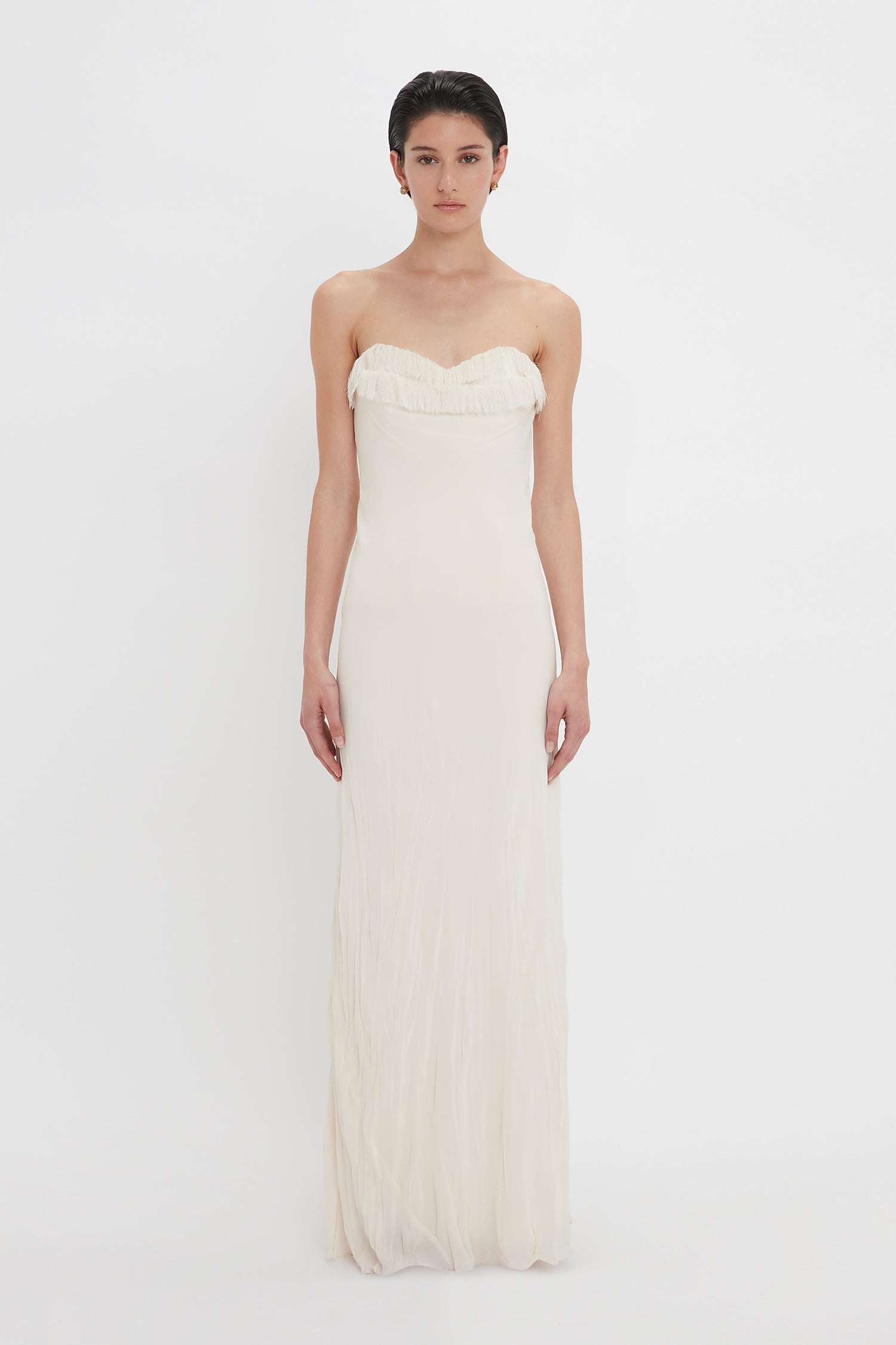 A woman in a strapless Victoria Beckham Exclusive Floor-Length Corset Detail Gown In Ivory stands against a plain white background, looking directly at the camera.