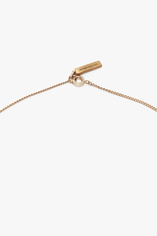 Close-up of an expertly handcrafted gold chain necklace with a small tag inscribed with "Victoria Beckham", showcasing the elegance of an Exclusive Camellia Flower Necklace In Gold.