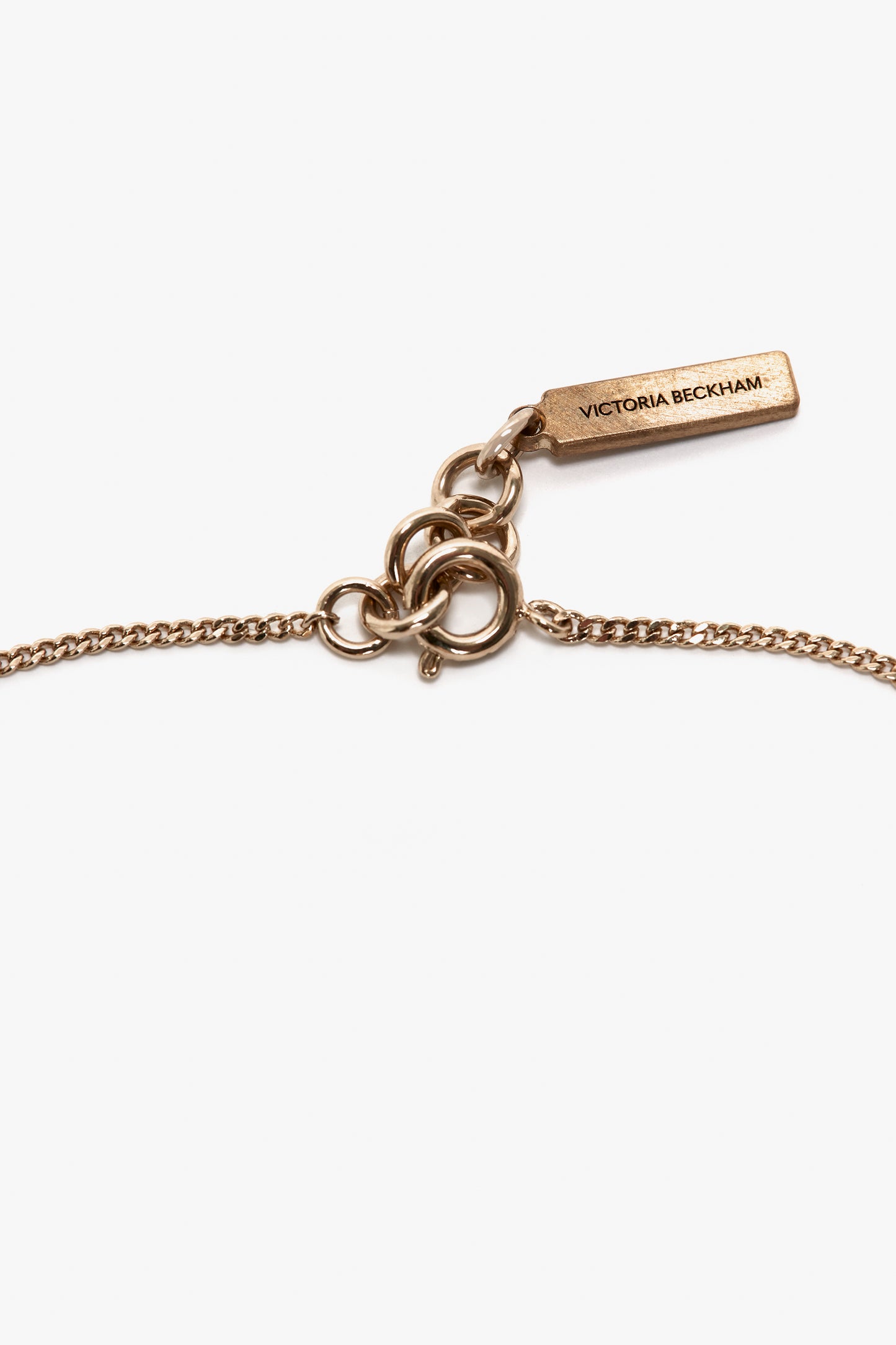 A delicate gold bracelet with an adjustable chain and clasp, featuring a rectangular tag inscribed with "Victoria Beckham," crafted in exquisite gold brushed brass.