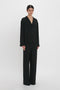 A person stands against a plain white background wearing the VB Monogram Pyjama Sleep Set In Black by Victoria Beckham.