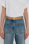 Person wearing a white short-sleeved top tucked into high-waisted blue jeans with large front pockets, fastened with a Frame Belt In Camel Leather by Victoria Beckham featuring luxury gold hardware.