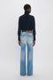 Person standing with back to the camera, wearing a navy turtleneck sweater and Alina High Waisted Jean In Light Summer Wash by Victoria Beckham reminiscent of vintage denim style.