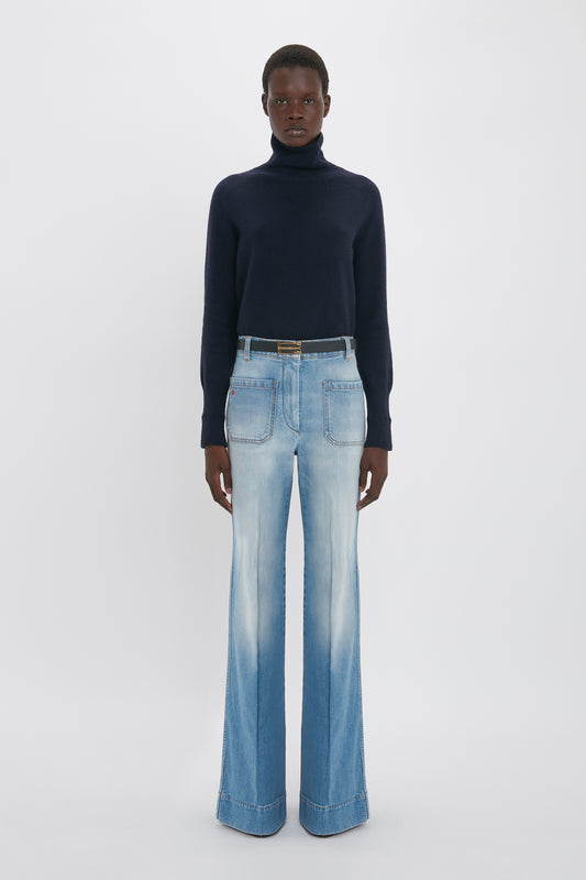 Person wearing a dark turtleneck and Alina High Waisted Jean In Light Summer Wash by Victoria Beckham stands against a plain white background.