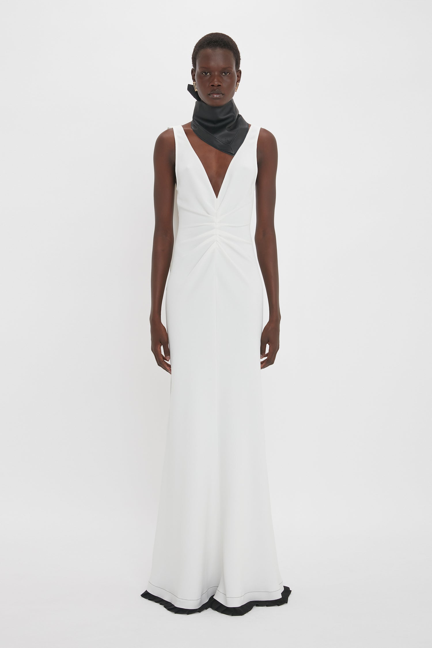 A person stands facing forward, wearing an elegant Exclusive V-Neck Gathered Waist Floor-Length Gown In Ivory by Victoria Beckham with a deep V-neck and a black neckpiece, accentuating the hourglass silhouette.