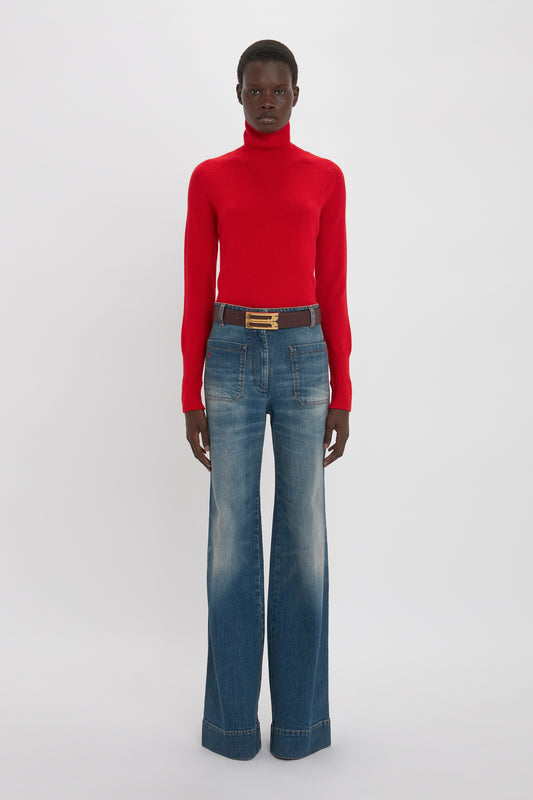 Person wearing a red turtleneck sweater and Victoria Beckham Alina High Waisted Jean In Heavy Vintage Indigo Wash, standing against a plain white background.