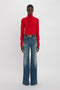 Person wearing a red turtleneck sweater and Victoria Beckham Alina High Waisted Jean In Heavy Vintage Indigo Wash, standing against a plain white background.