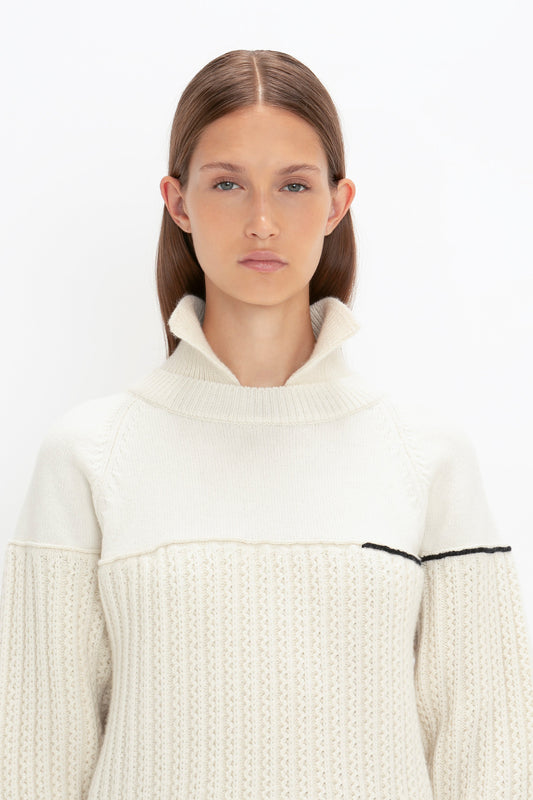 A person with long straight hair is wearing a Victoria Beckham Collar Detail Jumper In Natural featuring a high collar and black chain stitch detail on the sleeve. They are facing the camera against a plain white background.