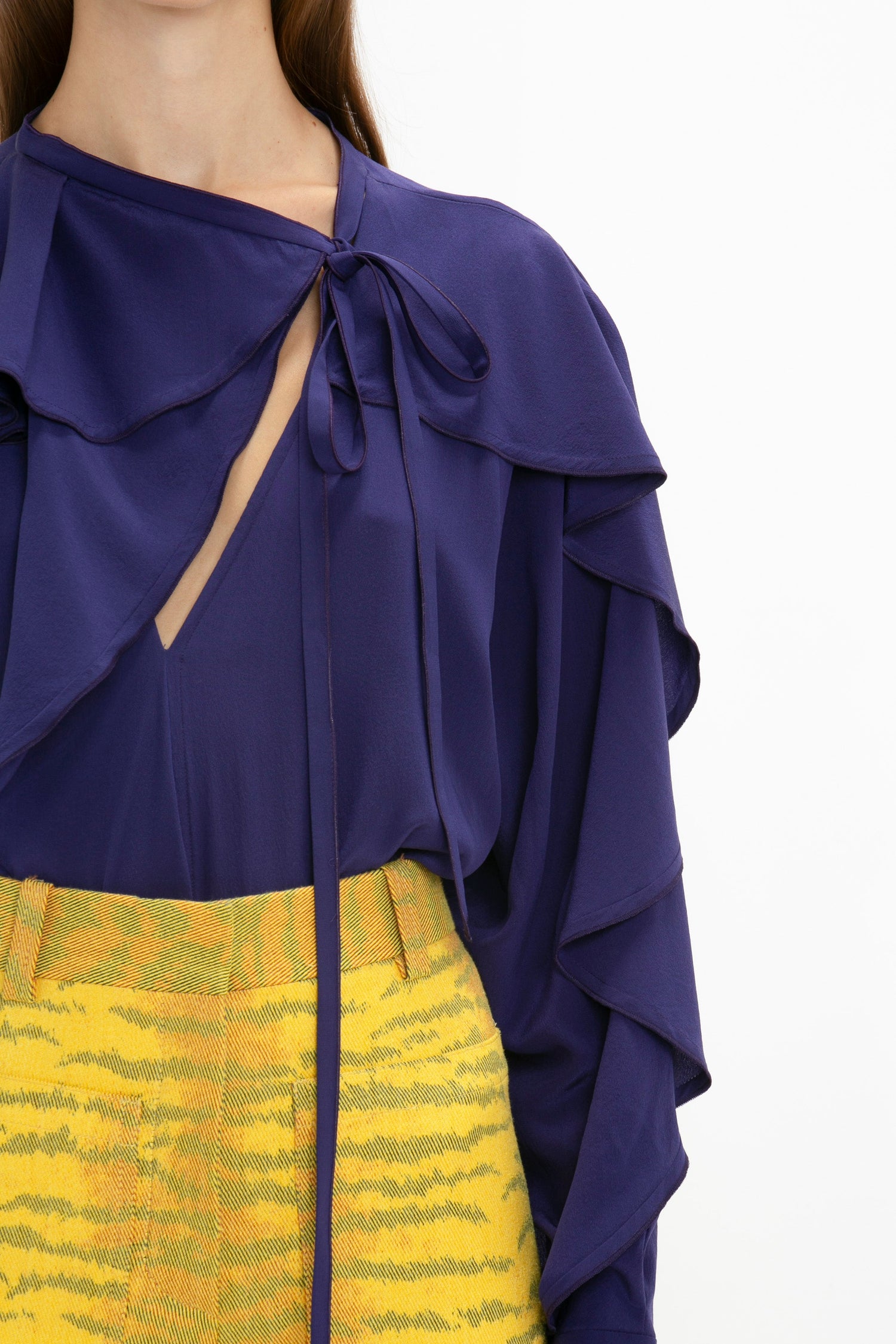 A person wearing a Victoria Beckham Tie Detail Ruffle Blouse In Ultraviolet paired with a yellow patterned skirt.