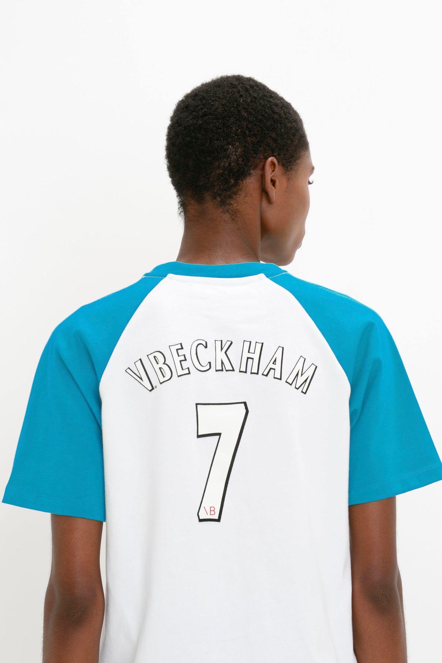 Person wearing a white and blue Exclusive Football T-Shirt In Blue from Victoria Beckham made from organic cotton with "VBECKHAM" and the number 7 on the back.