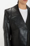 Close-up of a person wearing a black Victoria Beckham Tailored Leather Biker Jacket In Black crafted from calf leather over a white shirt. The jacket features a wide, angular collar and zipper detail, epitomizing the modern classic style.