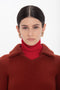 A woman with dark hair is wearing a Double Collared Jumper In Russet by Victoria Beckham and gold earrings, looking straight at the camera against a plain white background.